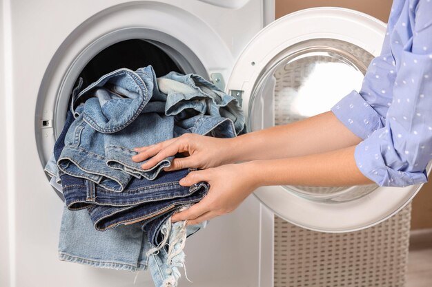 Woman putting dirty jeans and other denim clothes into washing machine closeup