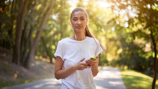 Woman putting on earphones to listen music before jogging summer park