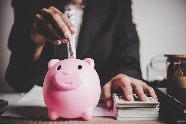 Woman putting euro banknote into a piggy bank on the table