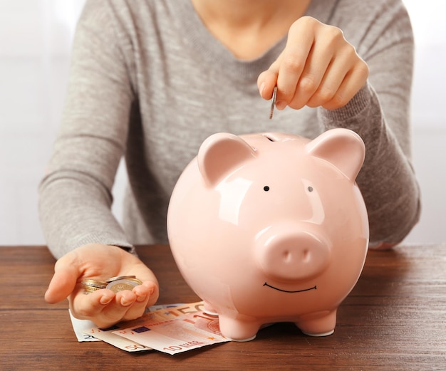 테이블에 있는 돼지 저금통에 유로 동전을 넣는 여자 금융 저축 개념