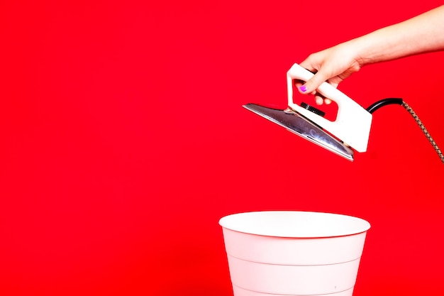 Photo woman putting iron in recycle bin on red background