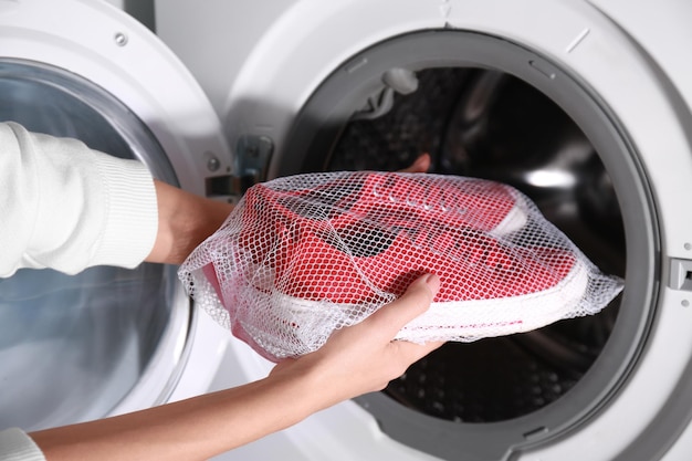 Woman putting mesh with red sneakers into washing machine closeup