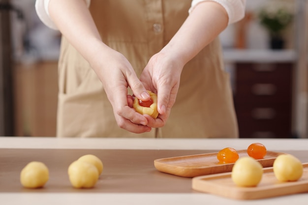 Woman putting salted egg yolk in th centre of the rolled-out dough when making mooncake