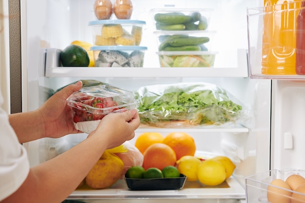 Woman putting strawberries in fridge