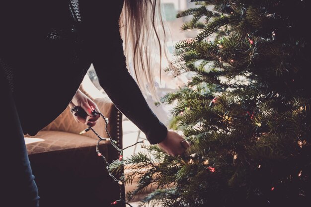 Photo woman putting string lights on christmas tree photo