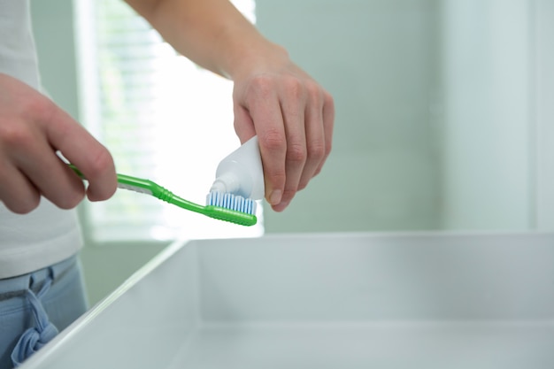 Woman putting toothpaste on brush in bathroom