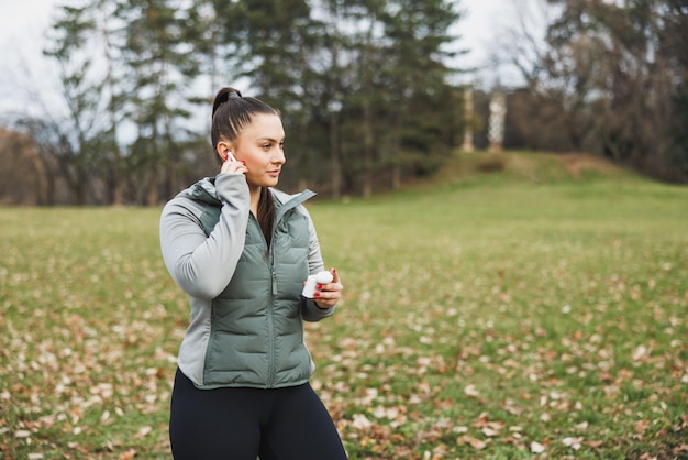 Woman Putting on Wireless Earbuds During an Outdoor Workout in the Park