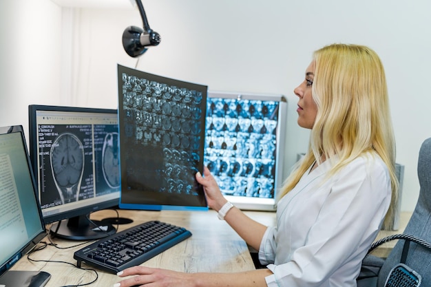 Женщина-рентгенолог держит рентгеновскую пленку возле компьютера Офисный фон Современное оборудование