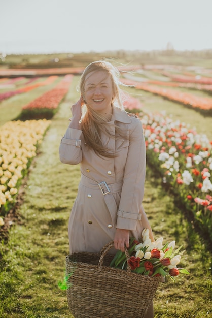 Woman in a raincoat at sunrise among the rows of tulips