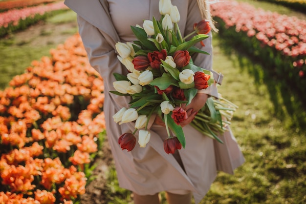 Woman in a raincoat at sunrise among the rows of tulips