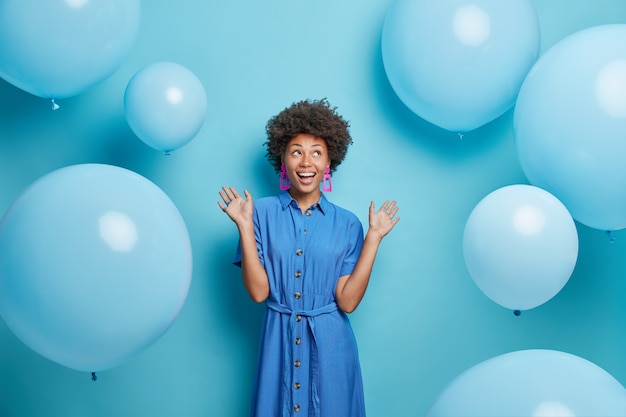 woman raises palms dressed in festive dress looks above isolated on blue