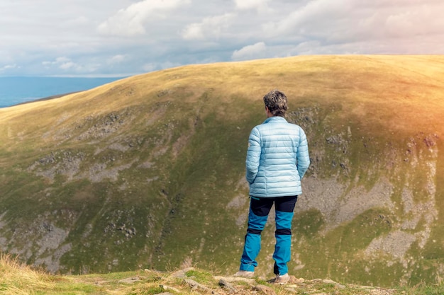 Woman reaching the destination and on the top of mountain against cloudy blue sky on autumn day T