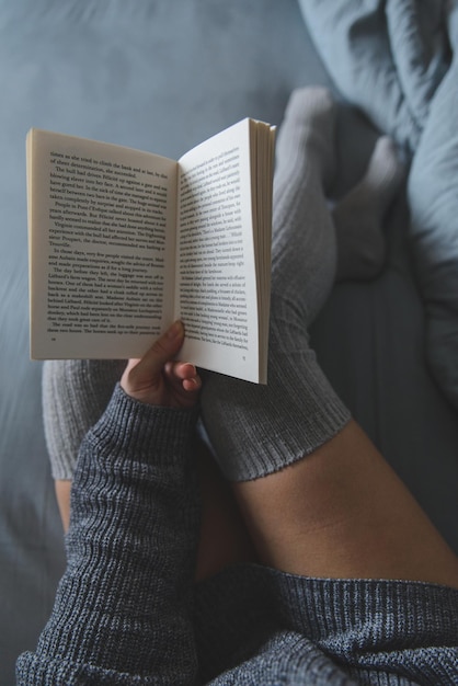 Woman read book in bed with grey sheets