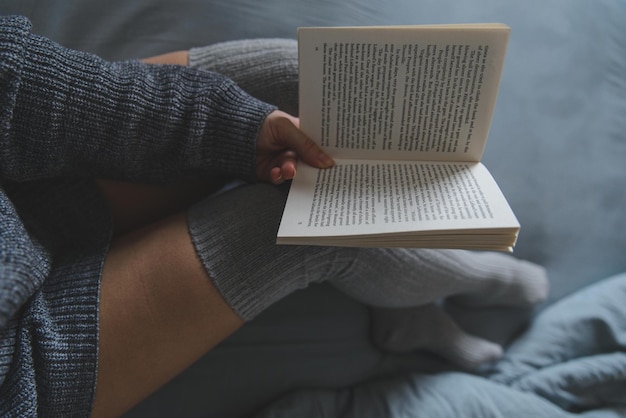 여자는 회색 시트와 함께 침대에서 책을 읽고