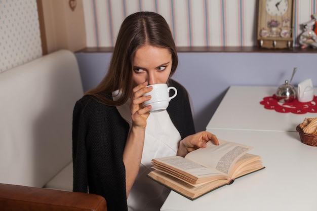 Woman reading book in cafe and drinking tea