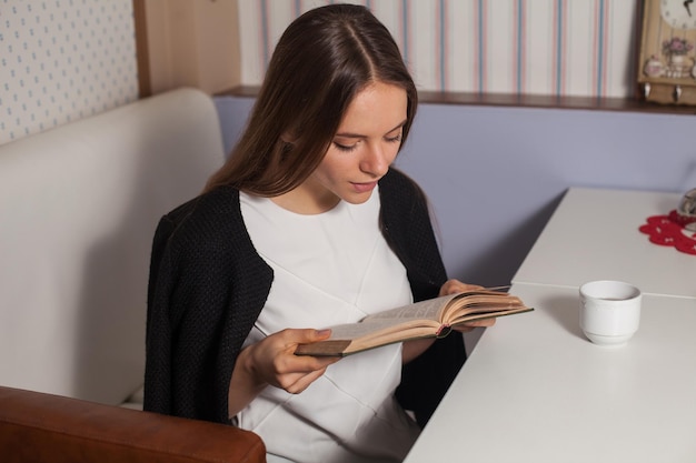 Woman reading book in cafe and drinking tea