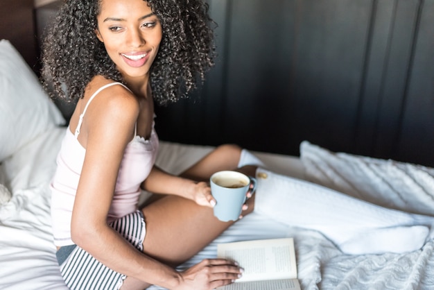 Woman reading a book and drinking coffee on bed with socks