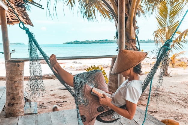 Woman reading book on hammock tropical beach, real people