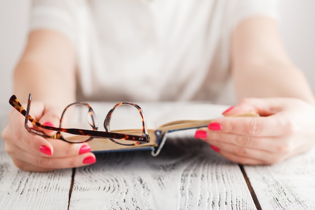 Woman reading a book and in her hand she holds a pair of eyeglasses