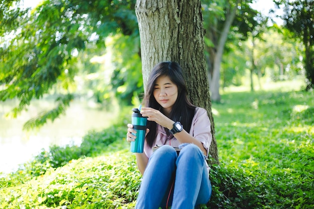 공원에서 책을 읽는 여자가을에 앉아 있는 아름다운 젊은 여성이 숲 속의 나무 아래 나뭇잎