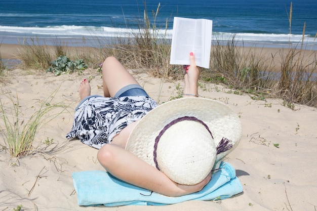 누워 있는 모래에 편안한 책을 읽는 여자