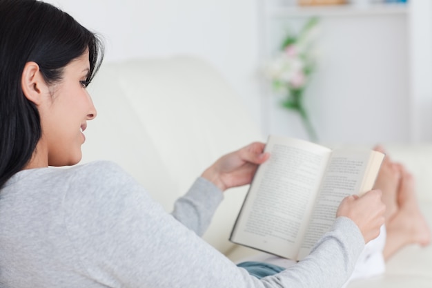 Woman reading a book while laying on a sofa