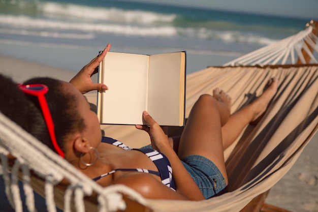 Foto donna che legge un libro mentre si rilassa sull'amaca sulla spiaggia