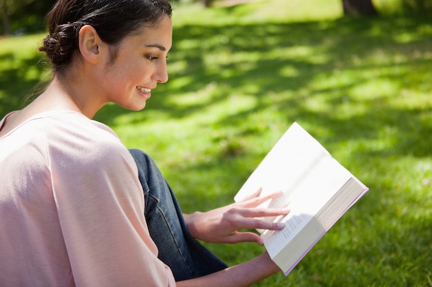 芝生に座っている間に本を読んでいる女性