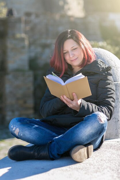 Photo woman reading book while sitting on railing