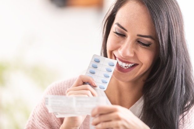 Woman reading a label of pills packaging, smiling.