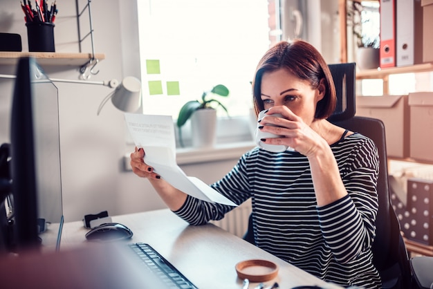 オフィスでメールを読んで、コーヒーを飲む女性