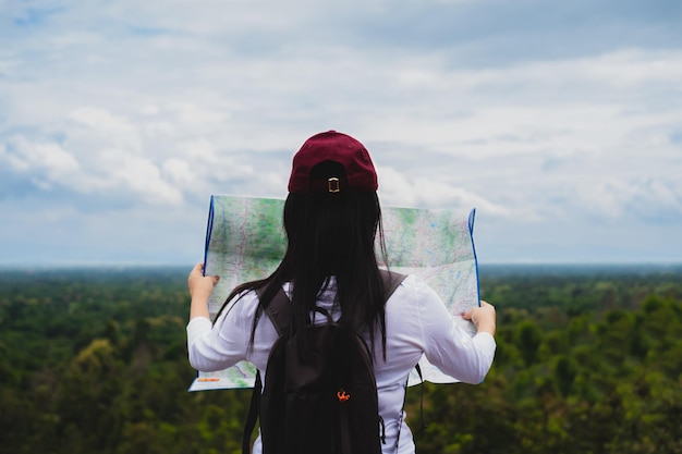 Woman reading map while standing in forest against sky