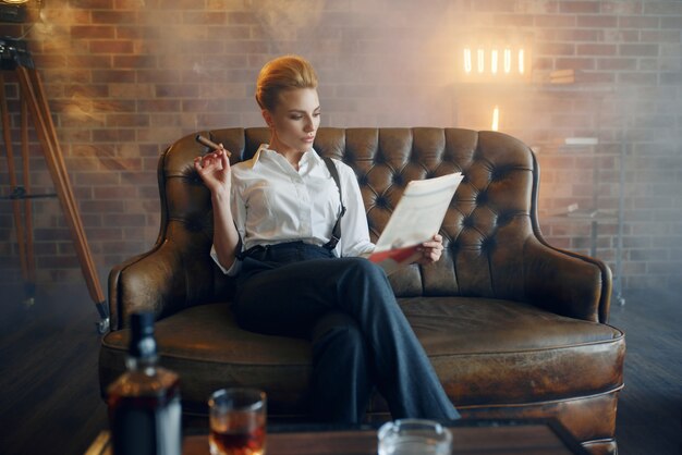 Woman reading newspapar with whiskey and cigar