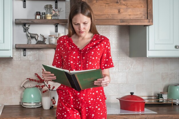 부엌 인테리어에서 요리책을 읽는 여성 가정 내부에서 요리책을 손에 든 여성