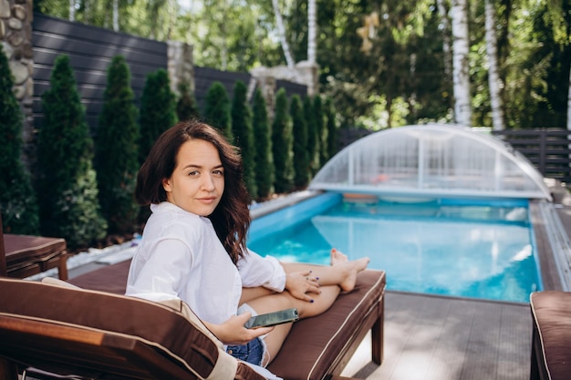 Woman reading and relaxing near luxury swimming pool