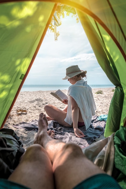 Woman reads a book on the beach near the tent