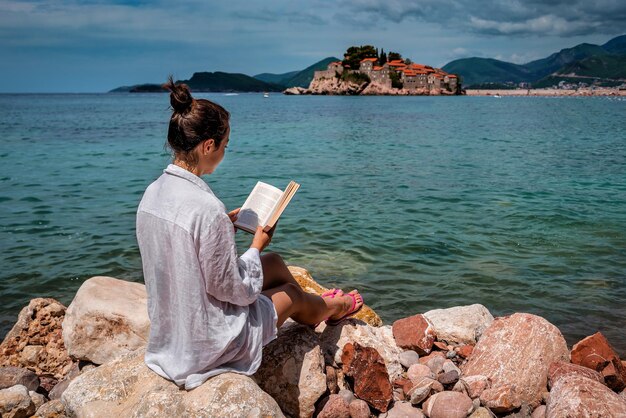 Woman reads the book on the sea shore in Sveti Stefan. Montenegro