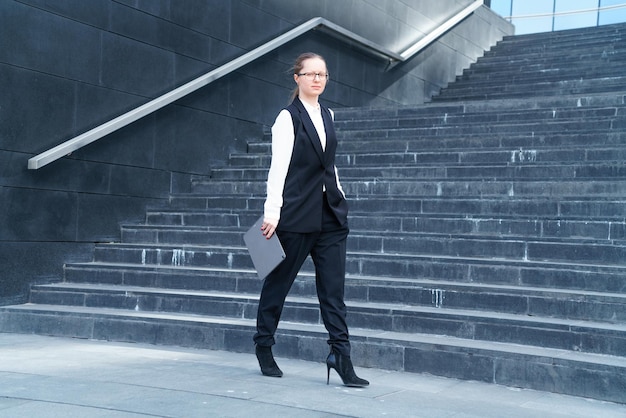 Woman realtor in jacket walks down stairs with laptop and phone in her hand