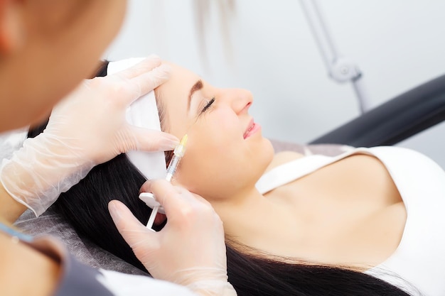 Woman receiving a botox injection in the lips zone lying in bathrobe on the medical couch