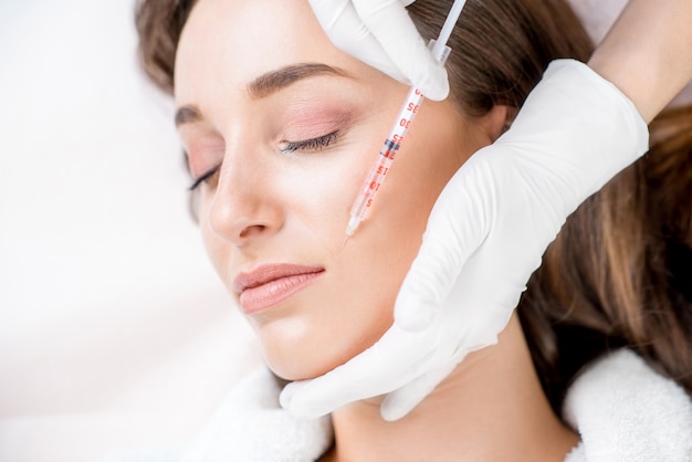 Woman receiving a botox injection in the lips zone lying on the medical couch