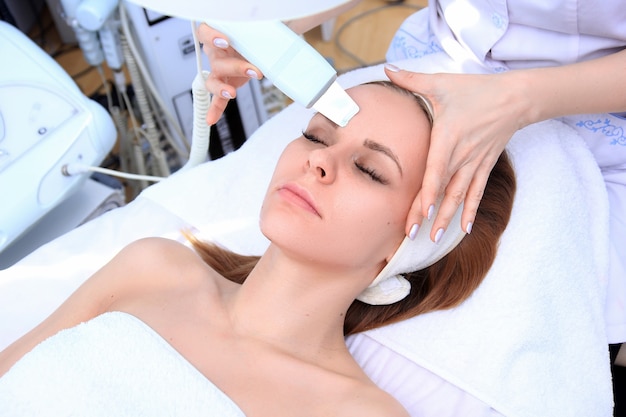 Женщина получает очищающую терапию с профессиональным ультразвуковым оборудованием в косметологическом кабинете