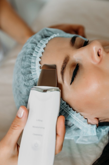 Woman receiving electric facial ultrasound peeling at beauty salon.