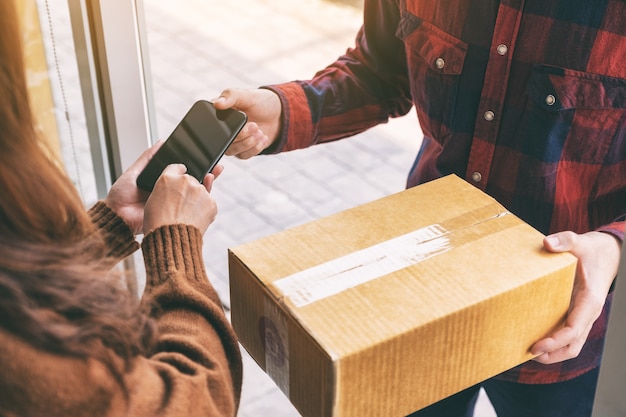 Photo woman receiving parcel box and signing name on the phone from delivery man at the house's door