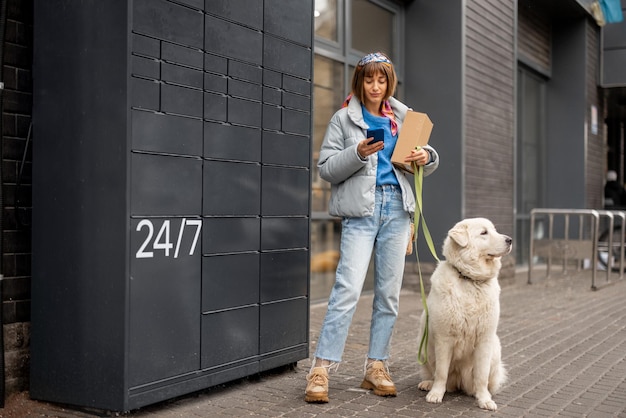 Woman receiving a parcel from automatic post machine during a walk with her dog