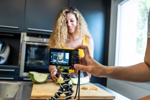 La registrazione della donna con una macchina fotografica gradisce una taglierina del melone in una cucina