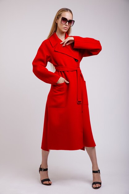 Foto donna in rosso cappotto autunnale occhiali da sole alla moda in posa su sfondo bianco studio shot slim figure