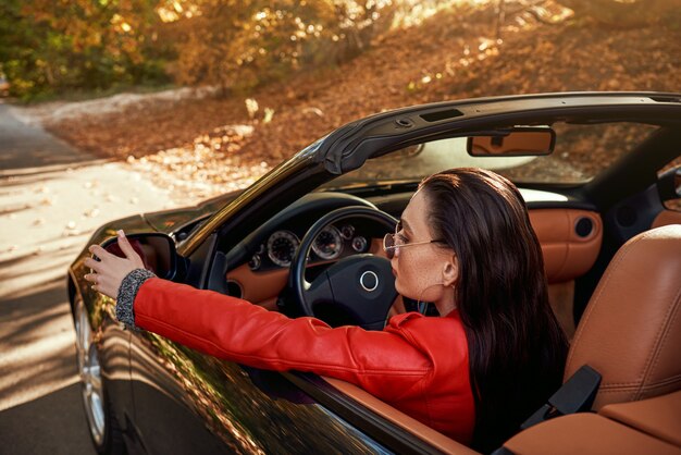 Woman in red in cabriolet she wearing sunglasses rear view