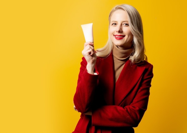 Woman in red coat with cream tube on yellow wall