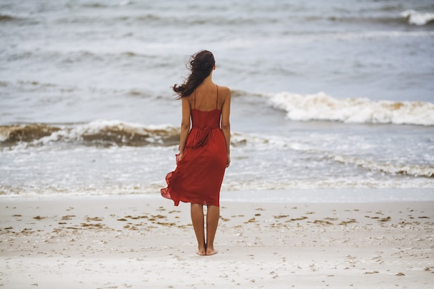 Woman in a red dress on the beach on a cold windy weather