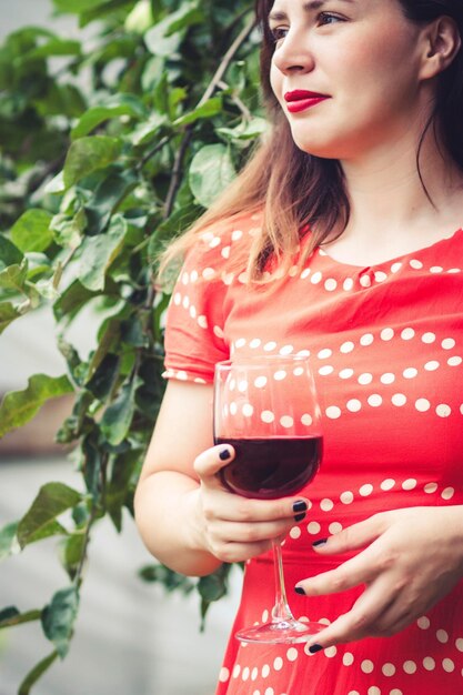 Foto donna in vestito rosso che beve vino rosso